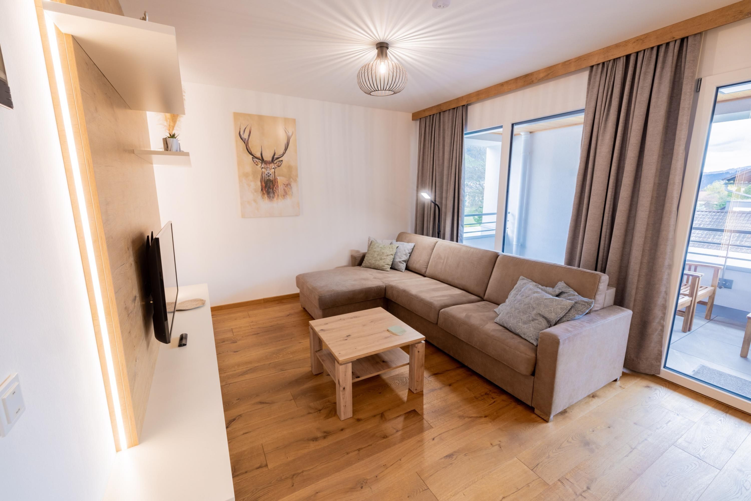 Un salon moderne avec un canapé d’angle, une table basse en bois et un téléviseur fixé au mur.
