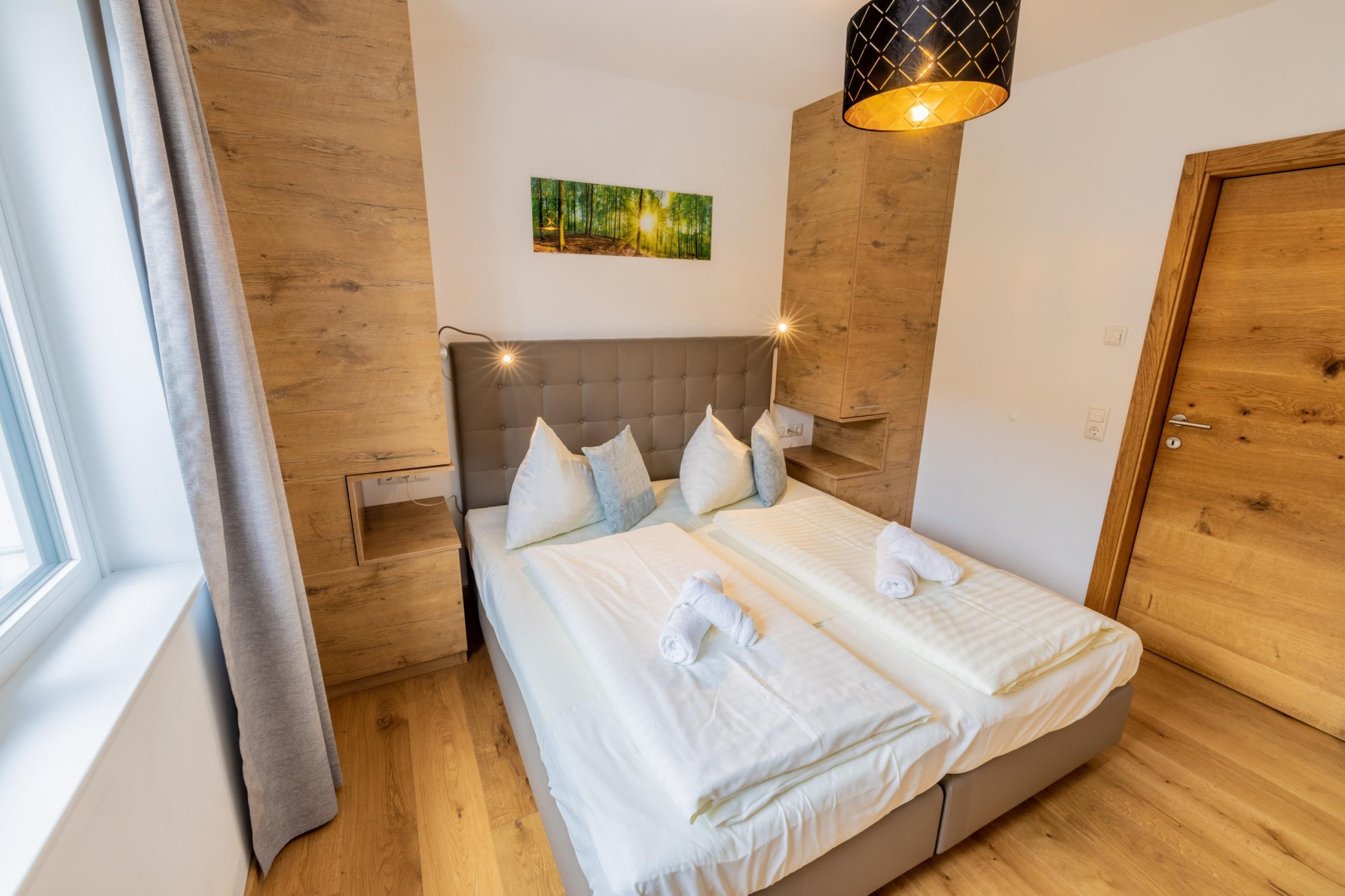 A double bed with white linens and pillows, a wooden headboard, a bedside table with a lamp, and a painting on the wall.