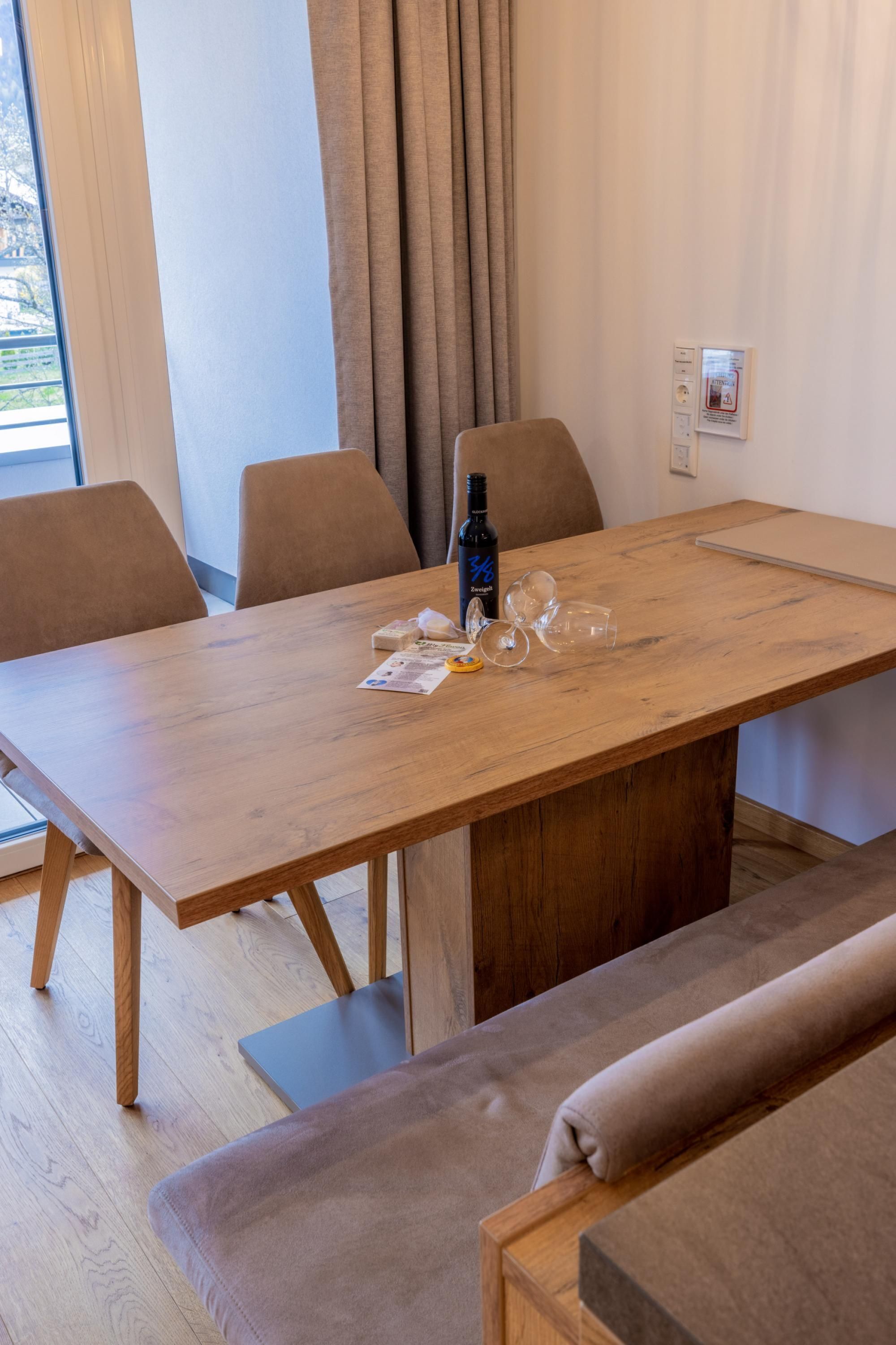 Een eethoek met een houten tafel, stoelen en een bank. Op de tafel staan een fles en glazen.