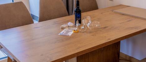 Een eethoek met een houten tafel, stoelen en een bank. Op de tafel staan een fles en glazen.