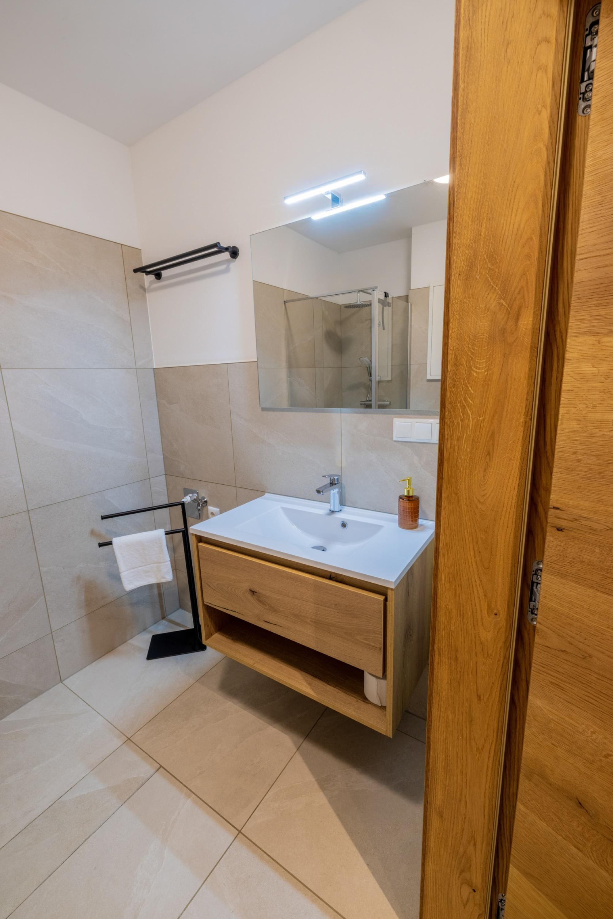 Un bagno moderno con un mobiletto in legno, uno specchio grande e un porta asciugamani.
