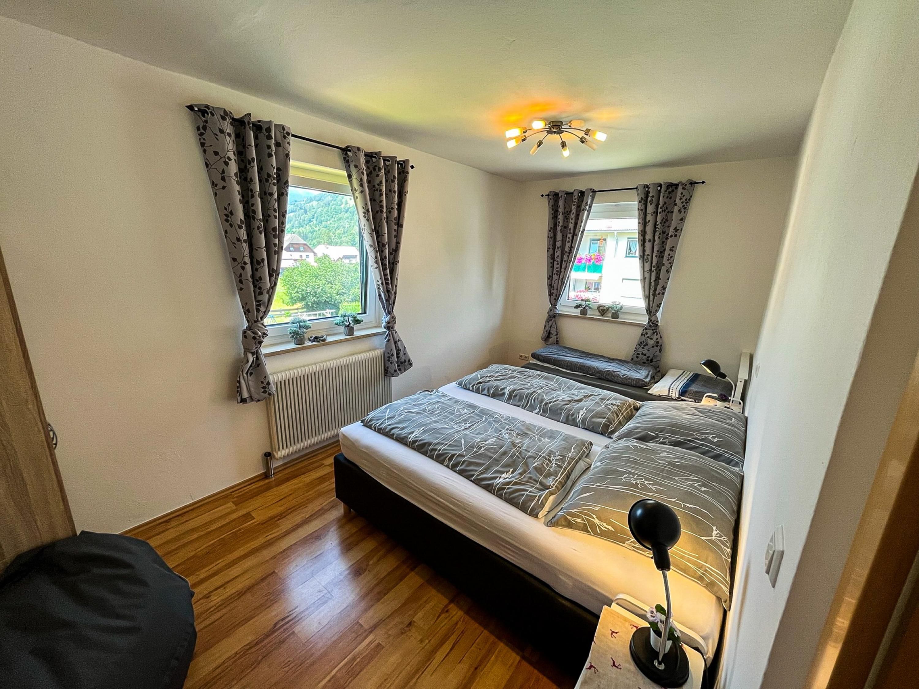 A bedroom with two beds, a radiator, a ceiling light, and windows with curtains.