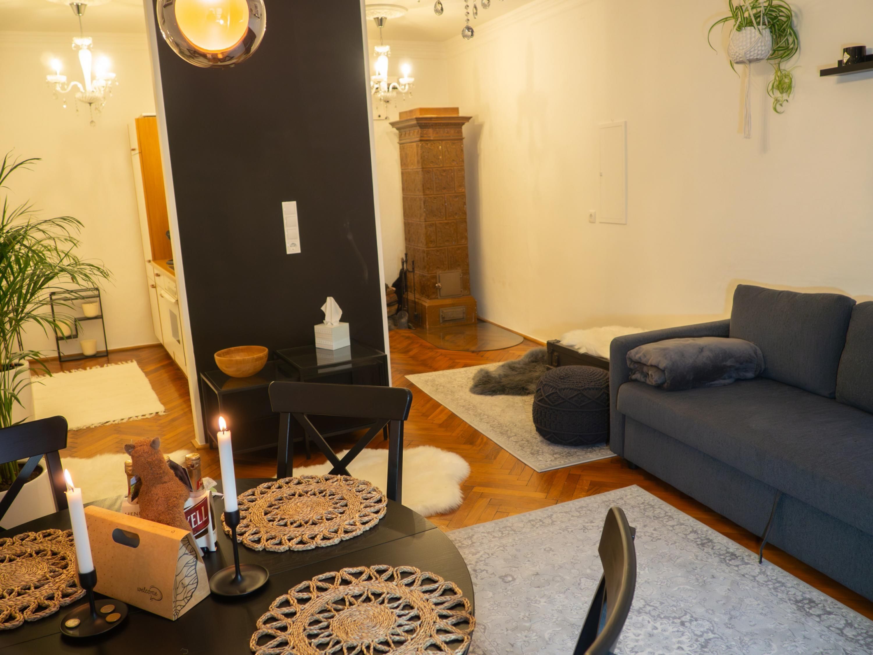 Ein gemütliches Wohnzimmer mit einer dunkel gefärbten Akzentwand, einem Kamin, einem grauen Sofa und einem Essbereich mit einem von Kerzen beleuchteten Tisch.