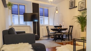 Een moderne woonkamer met een bank, poef, eettafel, stoelen en een kroonluchter.