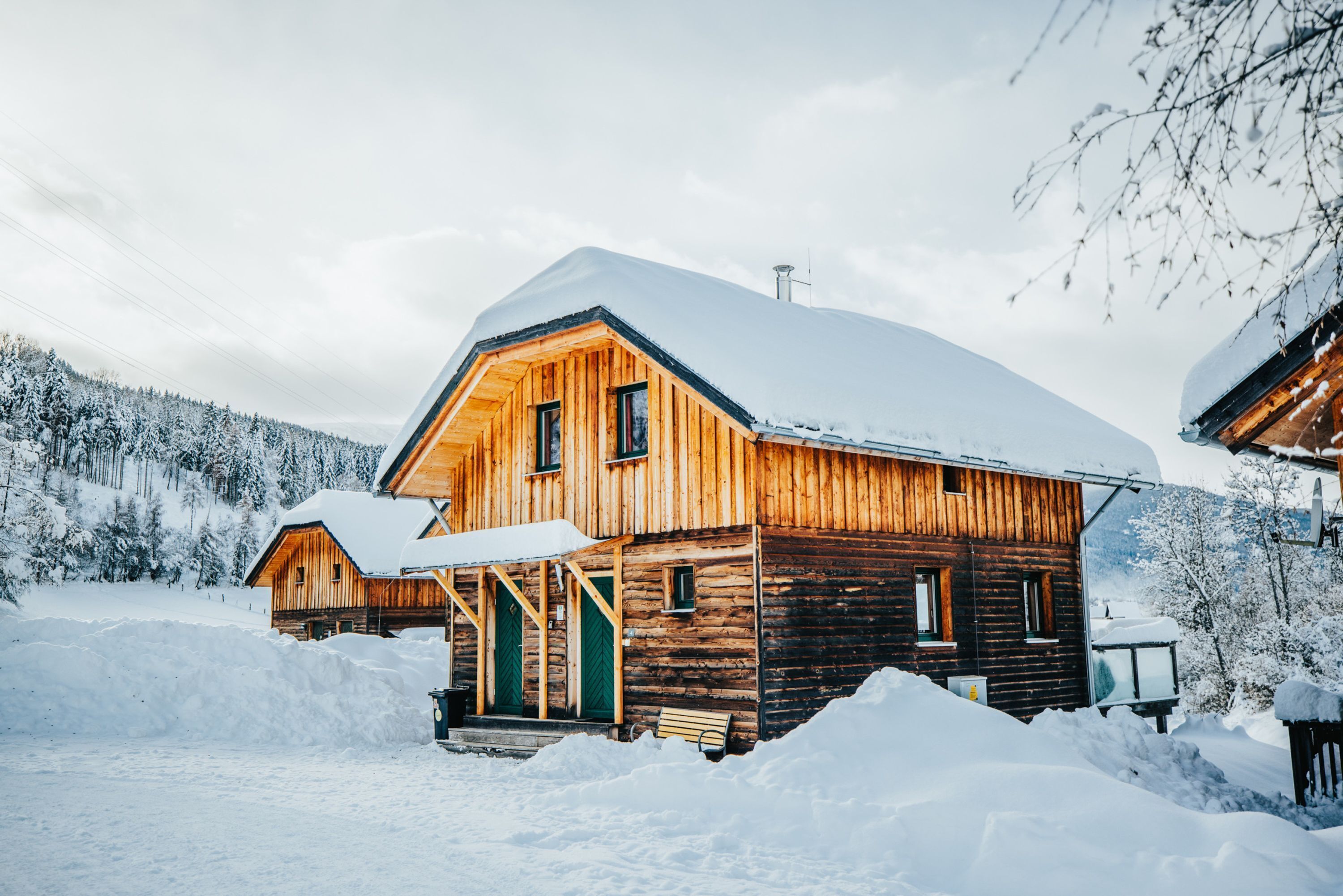A wooden cabin with a snow-covered roof, surrounded by snow and trees.