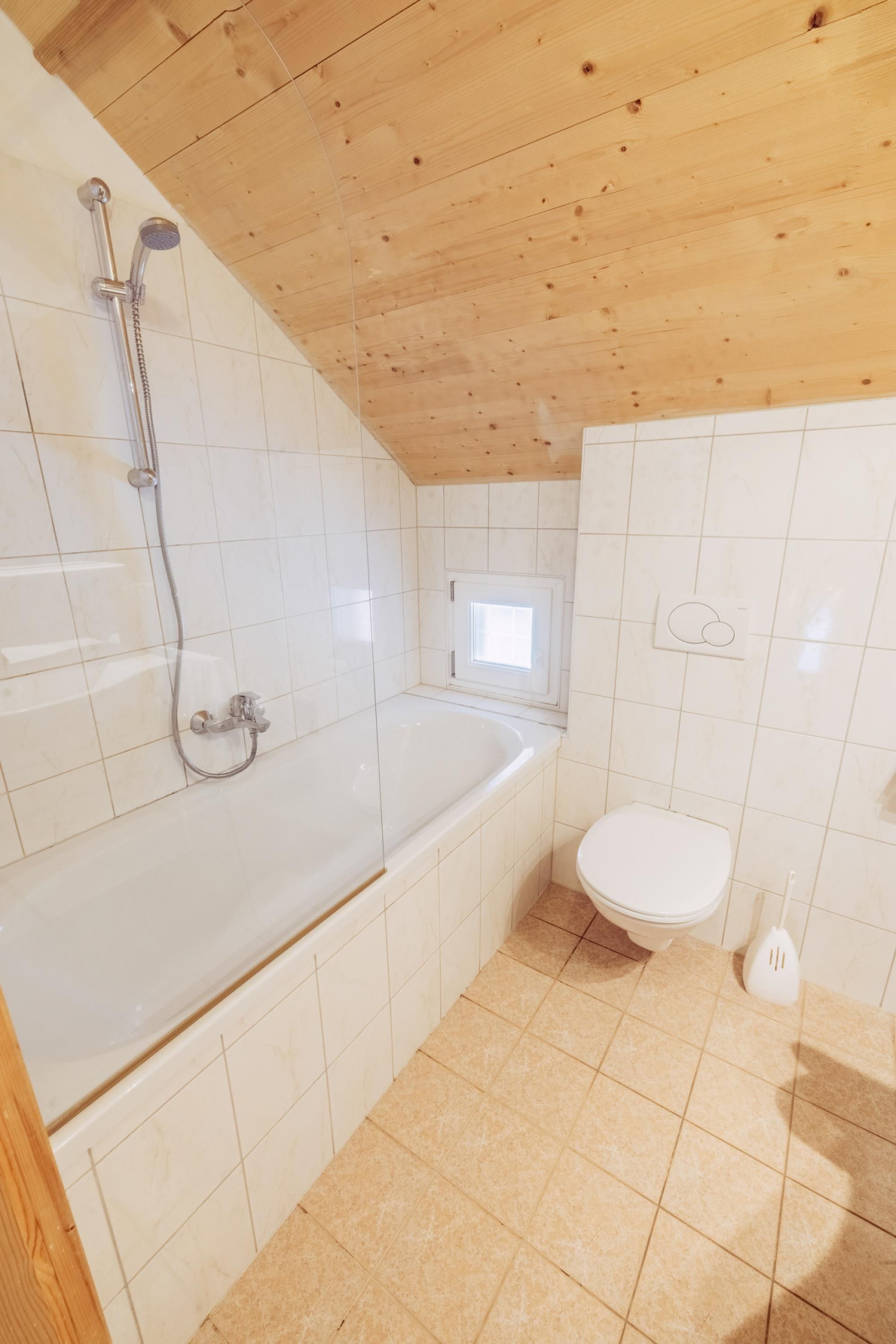 A small bathroom with a wooden ceiling, white tiles, a bathtub, and a toilet.