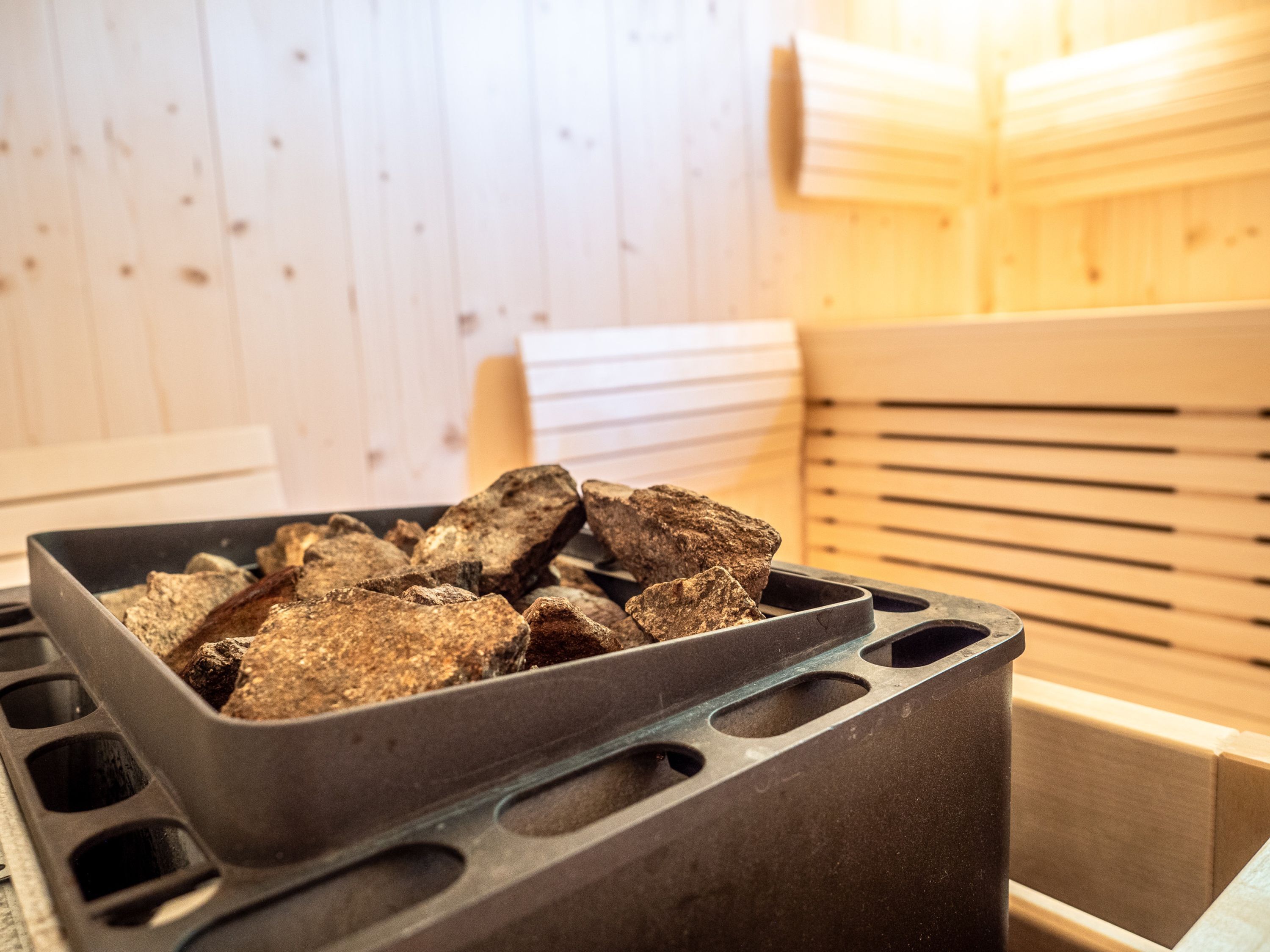 A sauna with wooden benches and a black container holding stones.
