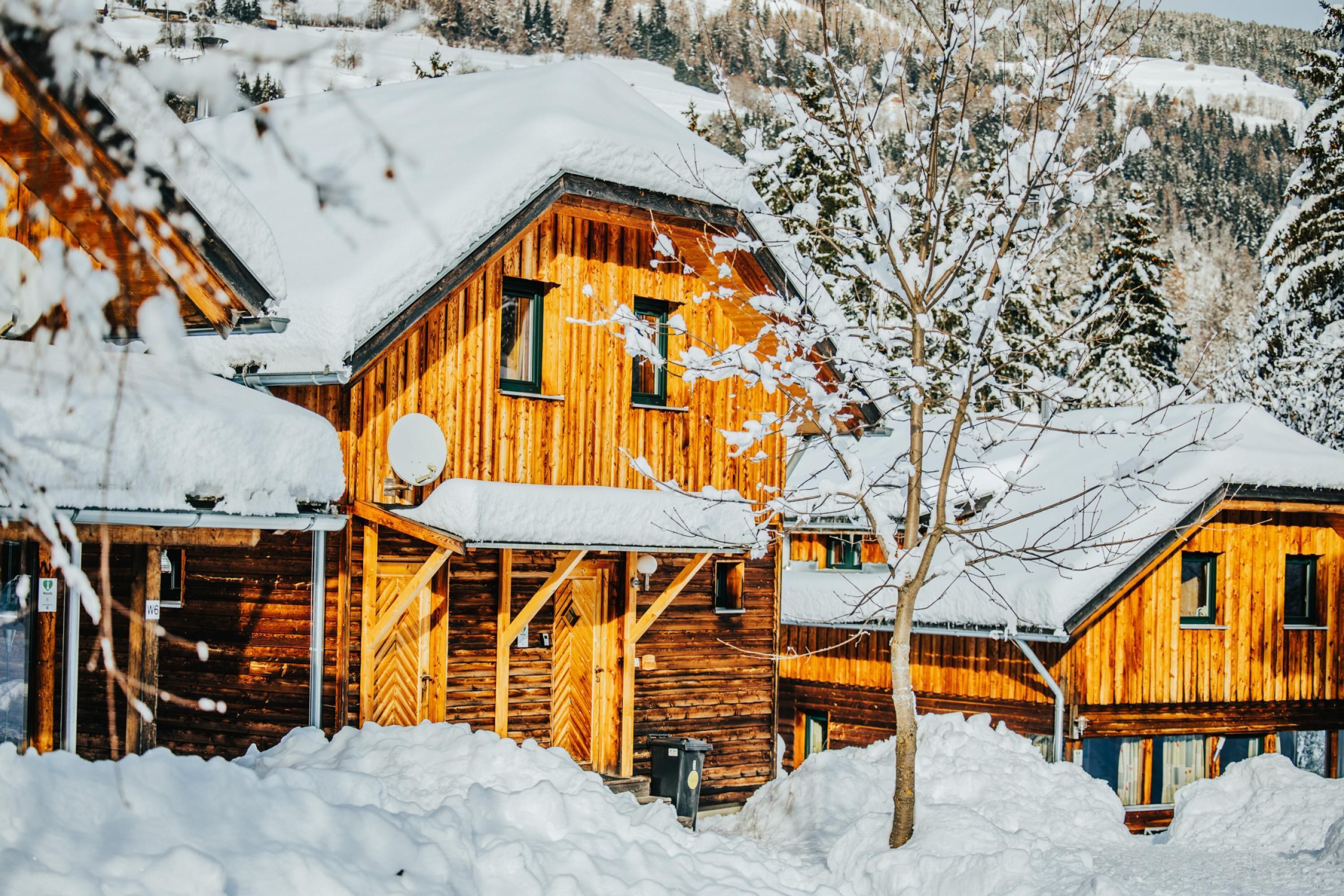 Una cabaña de madera con techo nevado, rodeada de nieve.