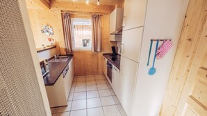 Una cucina funzionale e compatta con pareti in legno, pavimento piastrellato e servizi essenziali, tra cui un lavello, un piano cottura e pensili.