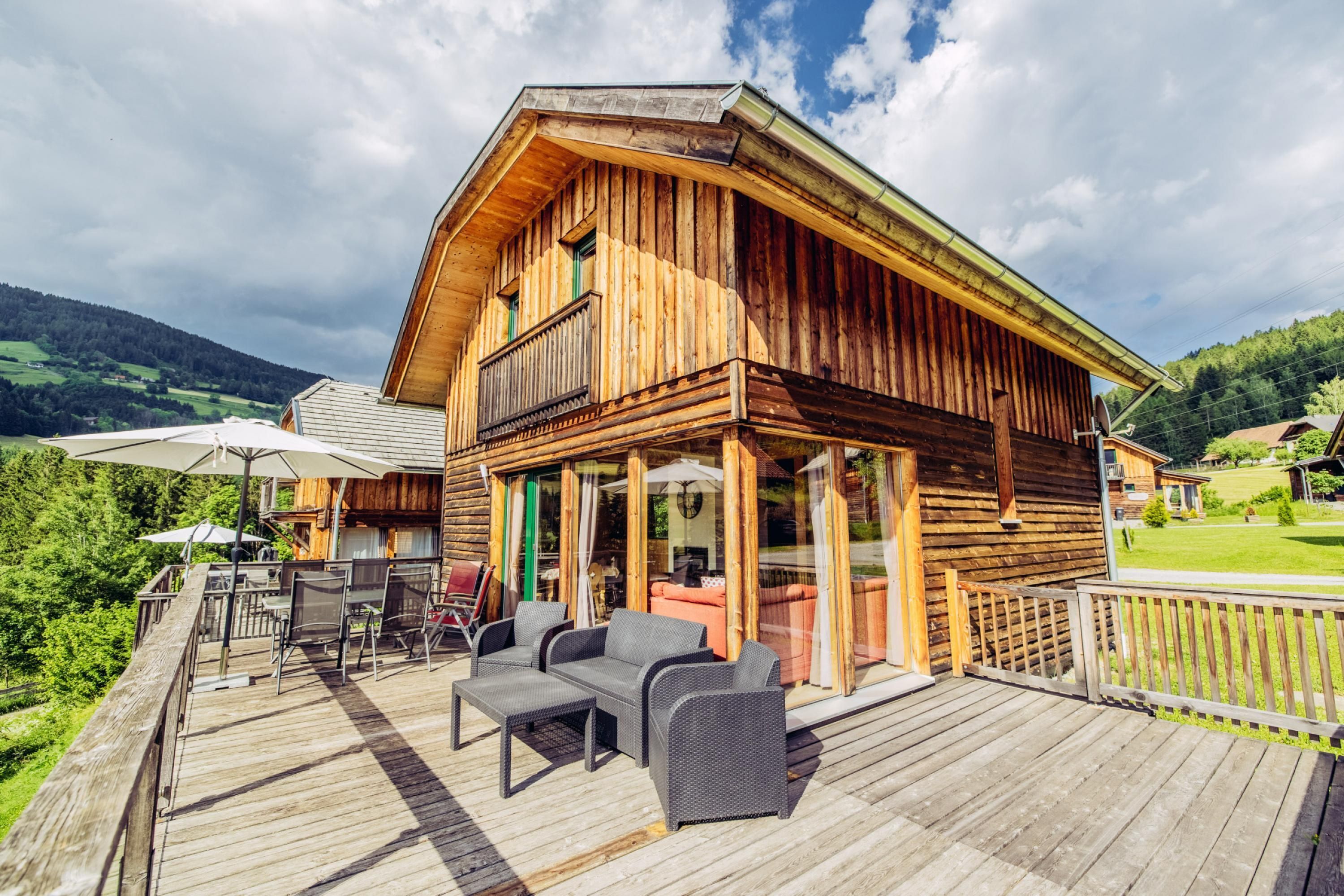 A wooden cabin with a deck, outdoor seating, and a view of the surrounding landscape.