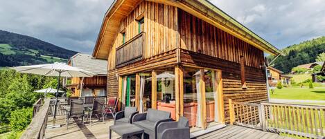 A wooden cabin with a deck, outdoor seating, and a view of the surrounding landscape.