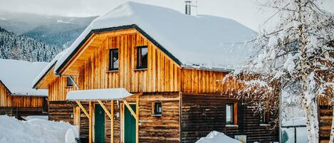 A wooden cabin with a green door, surrounded by snow.
