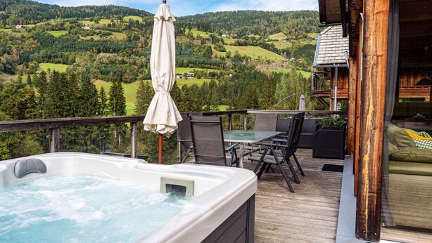 Un jacuzzi en una terraza de madera con vista a un valle boscoso.