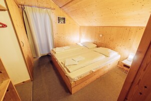 A wooden room with a bed, a nightstand, and a small table.