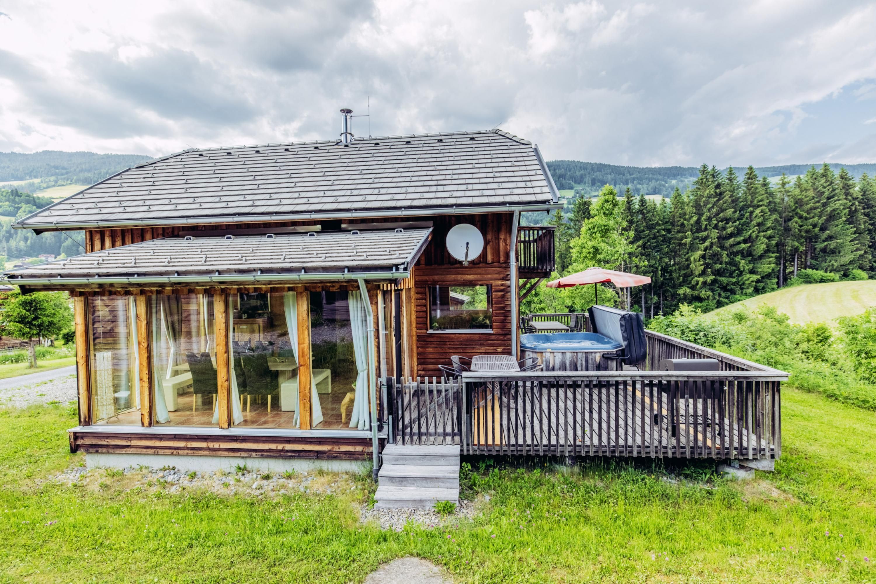 A wooden cabin with a deck, large windows, and a satellite dish.