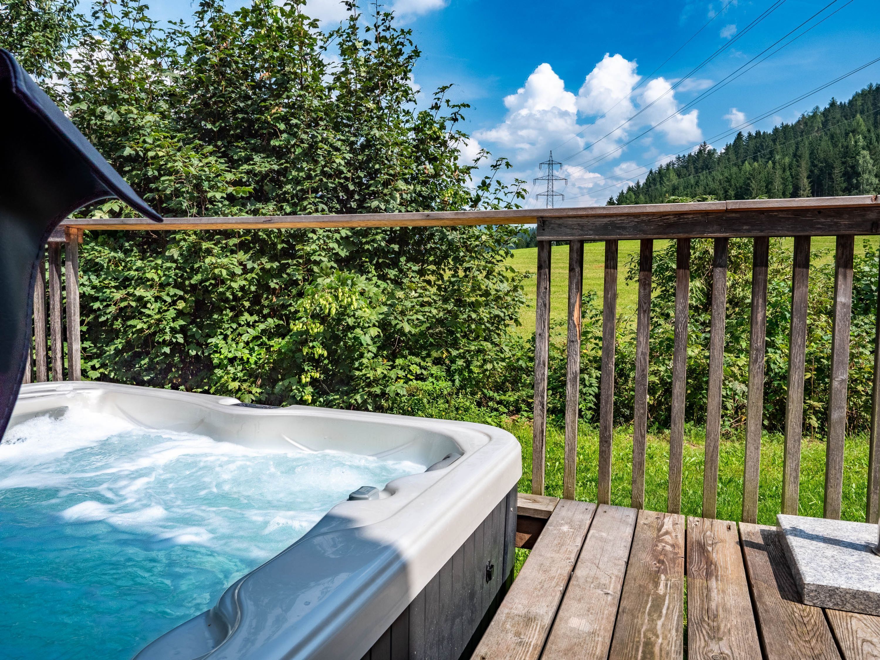 A hot tub on a wooden deck with a view of a forest and power lines.