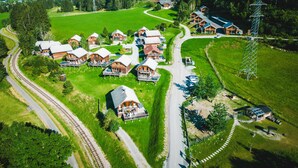 An aerial view of a rural village with wooden houses, a railway track, and a power pylon. - 034 W14 in St Georgen am Kreischberg (Sankt Georgen am Kreischberg)