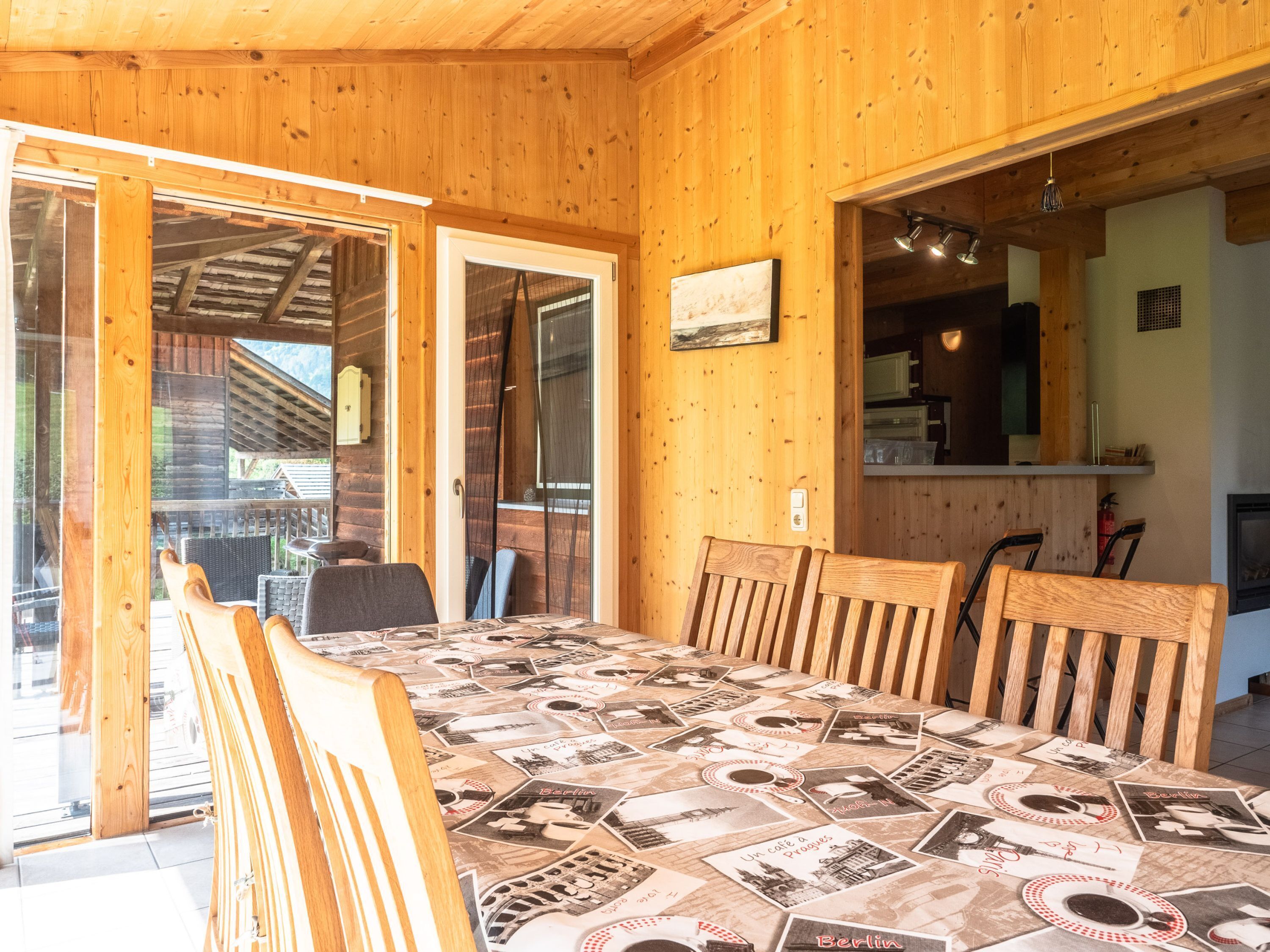 A wooden interior with a dining table covered in vintage postcards, wooden chairs, and a sliding glass door leading outside.