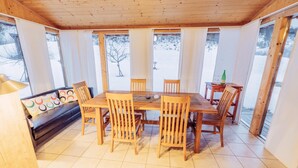 A wooden dining area with a table and chairs, large windows with curtains, and a view of a snowy landscape.