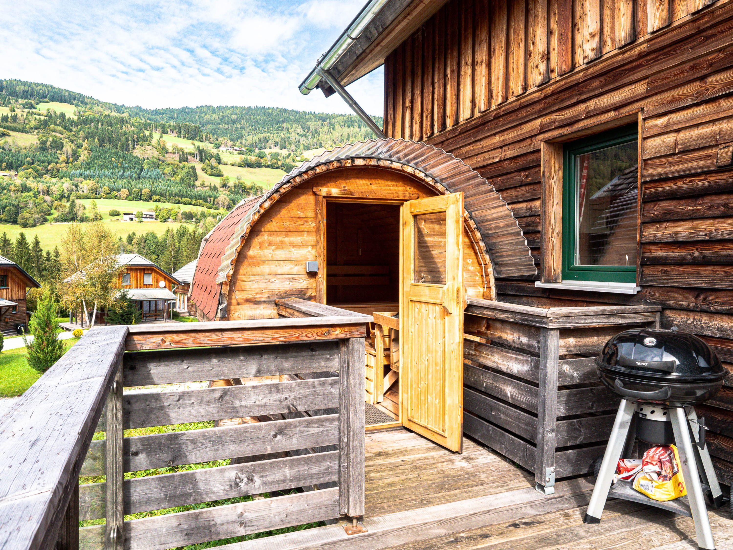 A wooden cabin with a wooden deck and a grill outside.