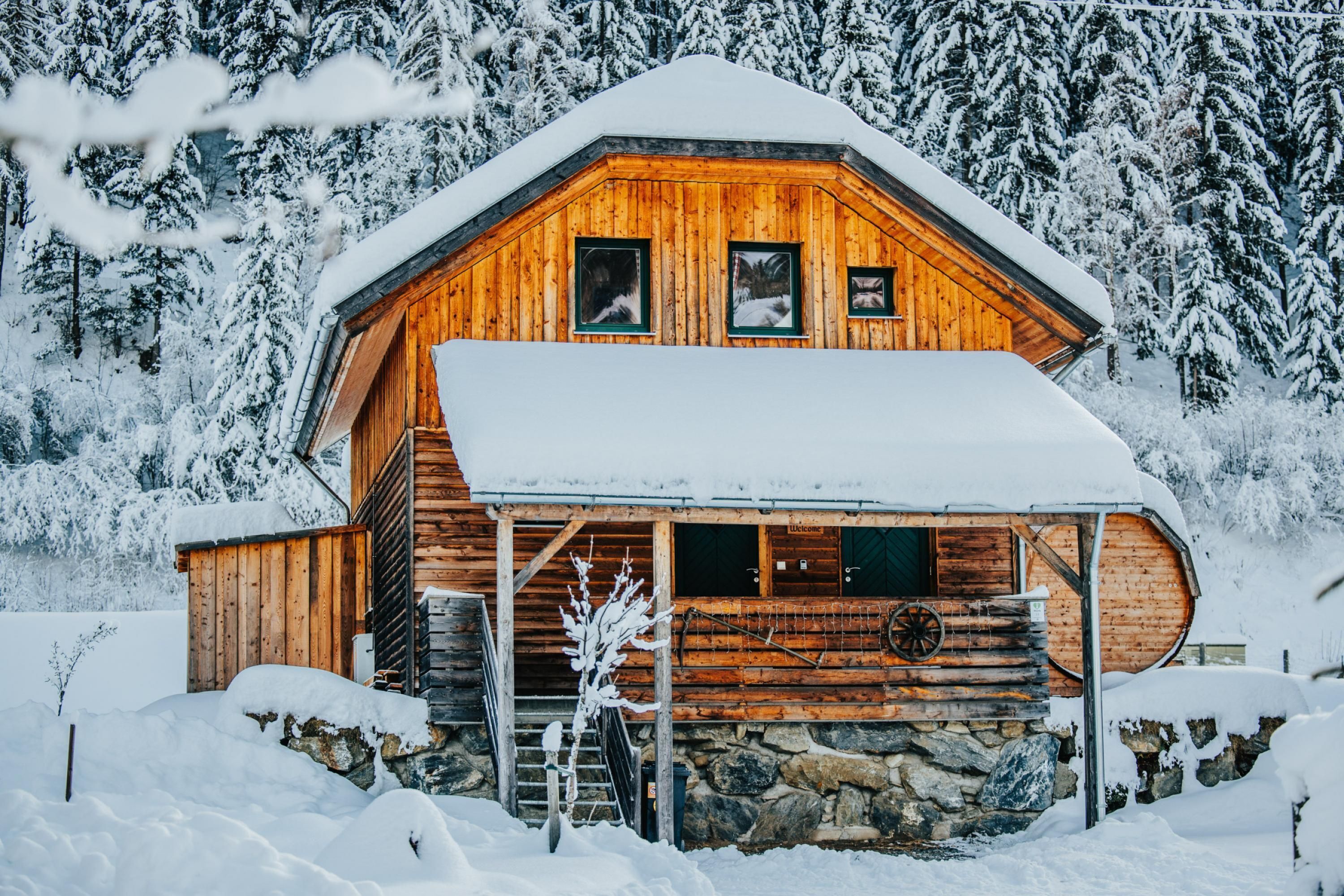 A wooden cabin with a stone foundation, surrounded by snow-covered trees.
