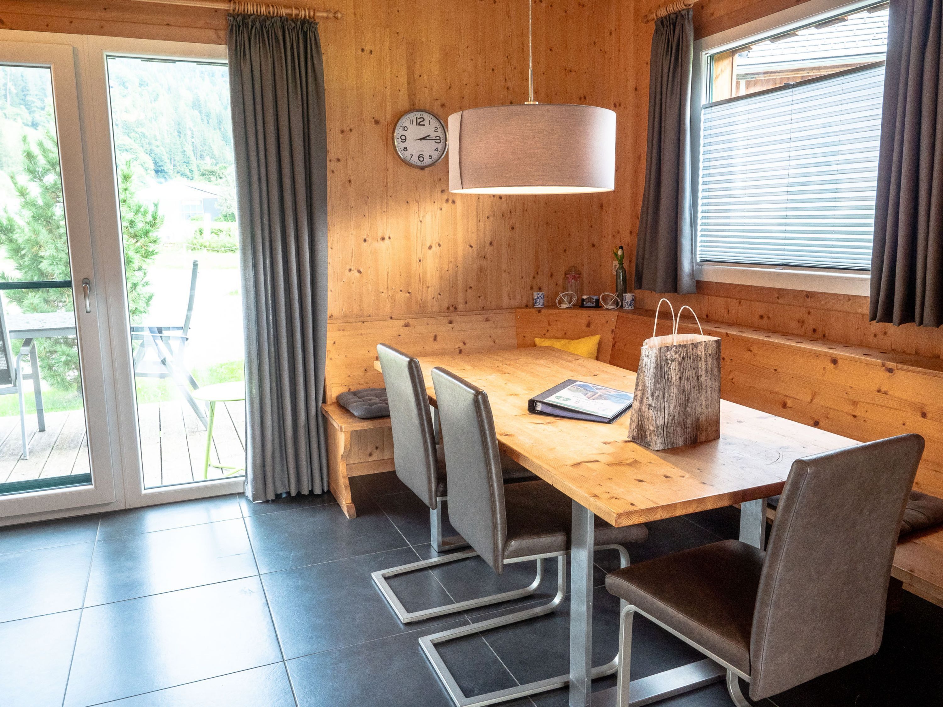 Un interior de madera con una mesa de comedor, sillas, un reloj y una ventana con cortinas.