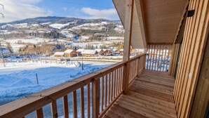 Un balcon en bois offrant une vue sur un paysage enneigé et sur des bâtiments situés au loin.