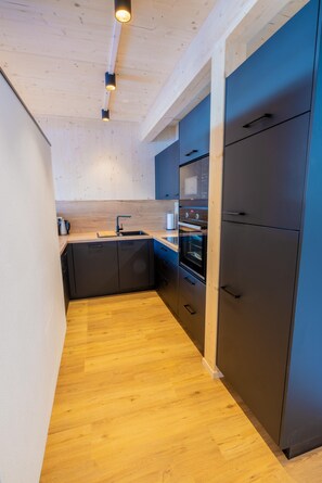 Una cocina moderna con vigas de madera en el techo, horno empotrado y un refrigerador grande.