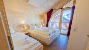 A wooden cabin bedroom with two beds, a balcony, and a view of the mountains.