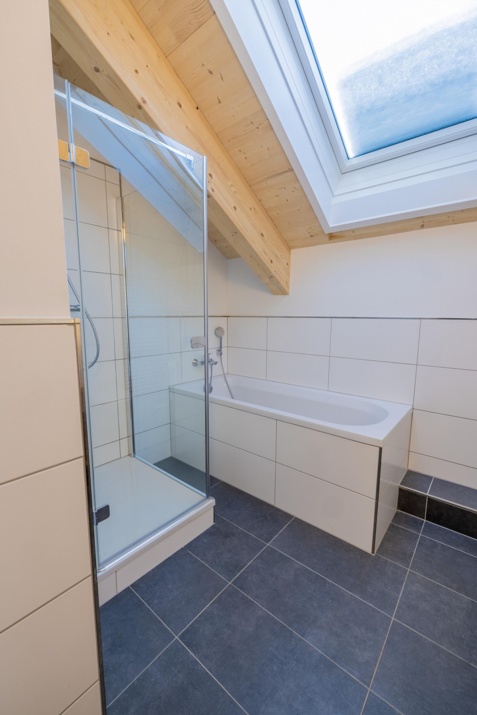 A modern bathroom with a glass shower enclosure, a bathtub, and a skylight.