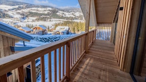 A wooden balcony with a view of snow-covered houses and mountains.
