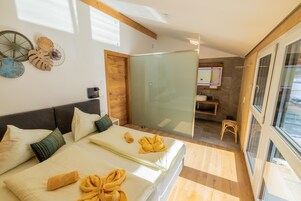 A modern hotel room with a large bed, a glass shower enclosure, and a view through the glass door.