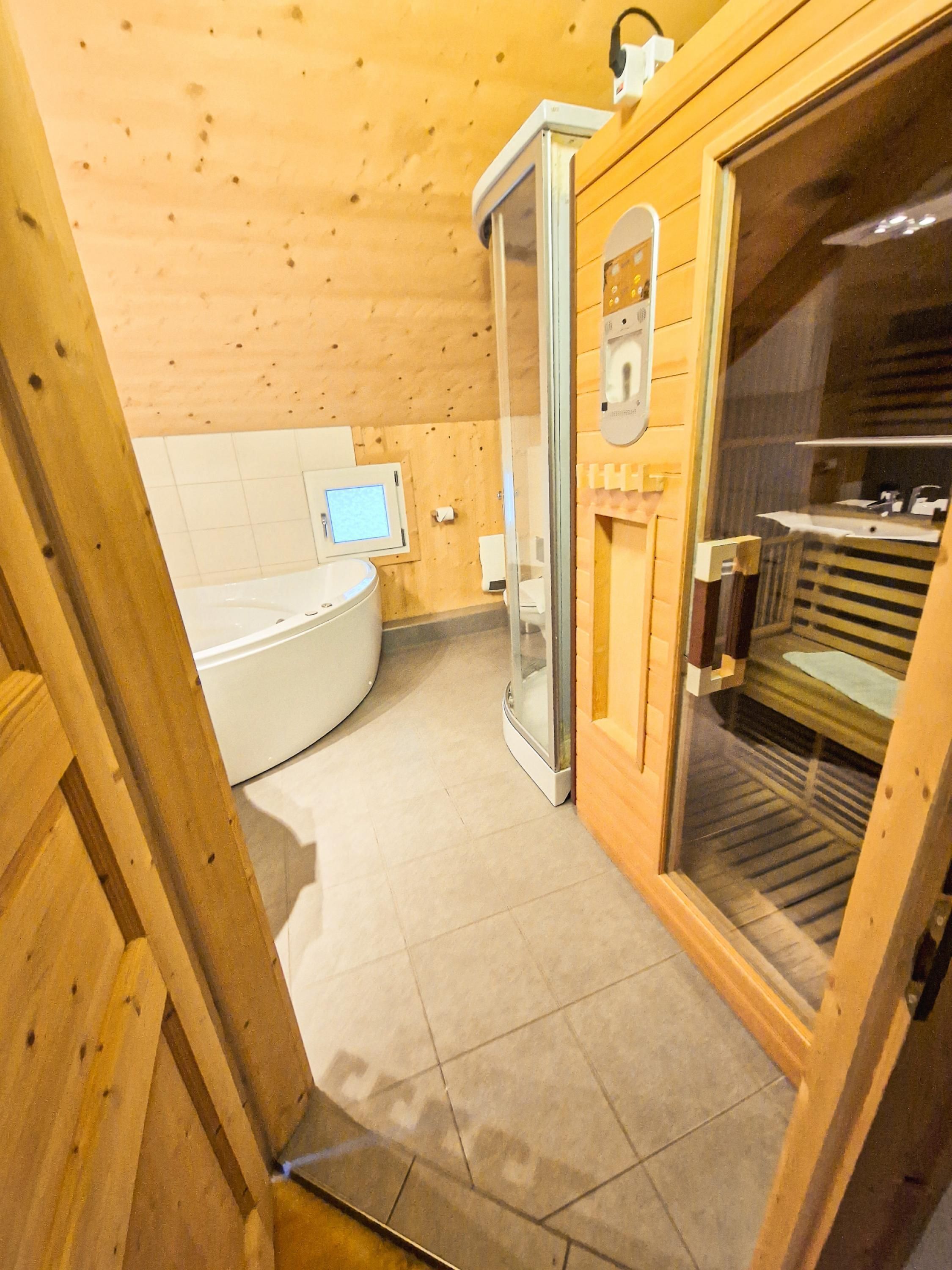 Un intérieur en bois avec un sauna, une porte en verre et une baignoire blanche.