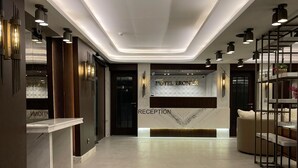 A hotel reception area with a modern design, featuring a reception desk, a reception sign, and a seating area with a sofa and a coffee table. - Hotel Eronur (Bilecik)