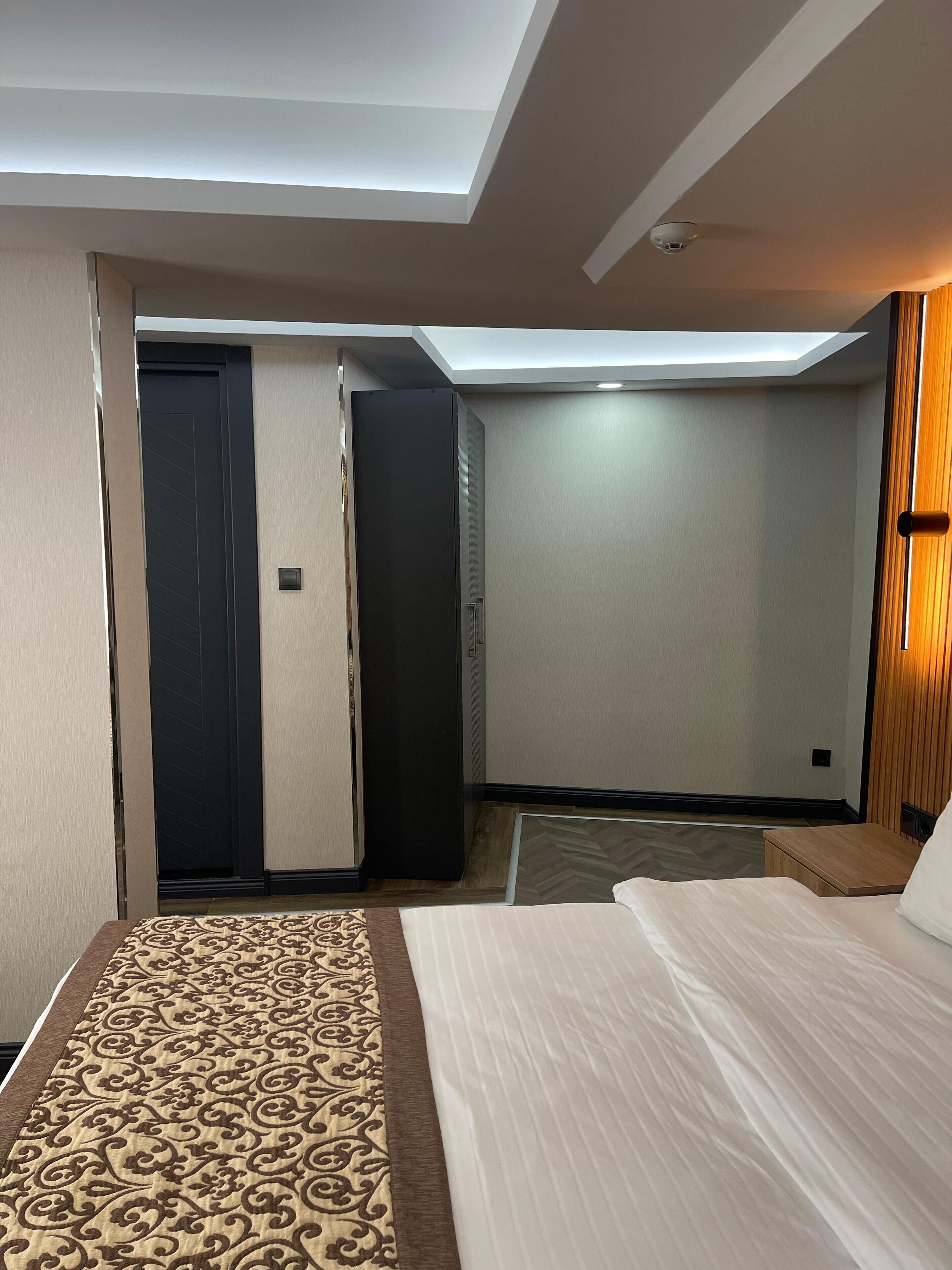 Una habitación de hotel con cama, armario, escritorio y una lámpara en el techo.