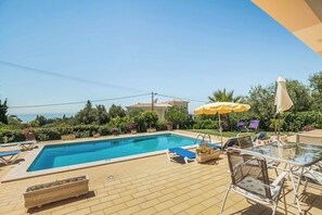 A rectangular swimming pool with a tiled deck, surrounded by lounge chairs and umbrellas.
