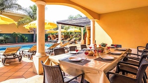 An outdoor dining area with a pool view, covered by a pergola, and furnished with tables and chairs. - Villa Cabrita de Parra (Albufeira)
