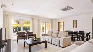 A modern living room with a sofa, armchairs, a coffee table, and a TV. There is a dining area with a table and chairs. - Villa Cabrita de Parra (Albufeira)