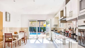 A modern kitchen with a dining area, a pool view, and a sliding glass door leading to the outdoor area. - Villa Cabrita de Parra (Albufeira)