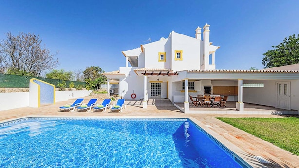 A two-story house with a swimming pool, a patio with lounge chairs, and a covered outdoor dining area. - Villa Cordyline (Albufeira)