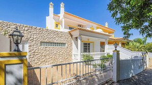 A white building with yellow accents, a stone wall, and a cobblestone pathway leading to a gated entrance. - Villa Cordyline (Albufeira)