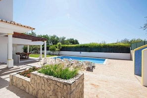 An outdoor swimming pool area with a pergola, stone planters, and a covered seating area.