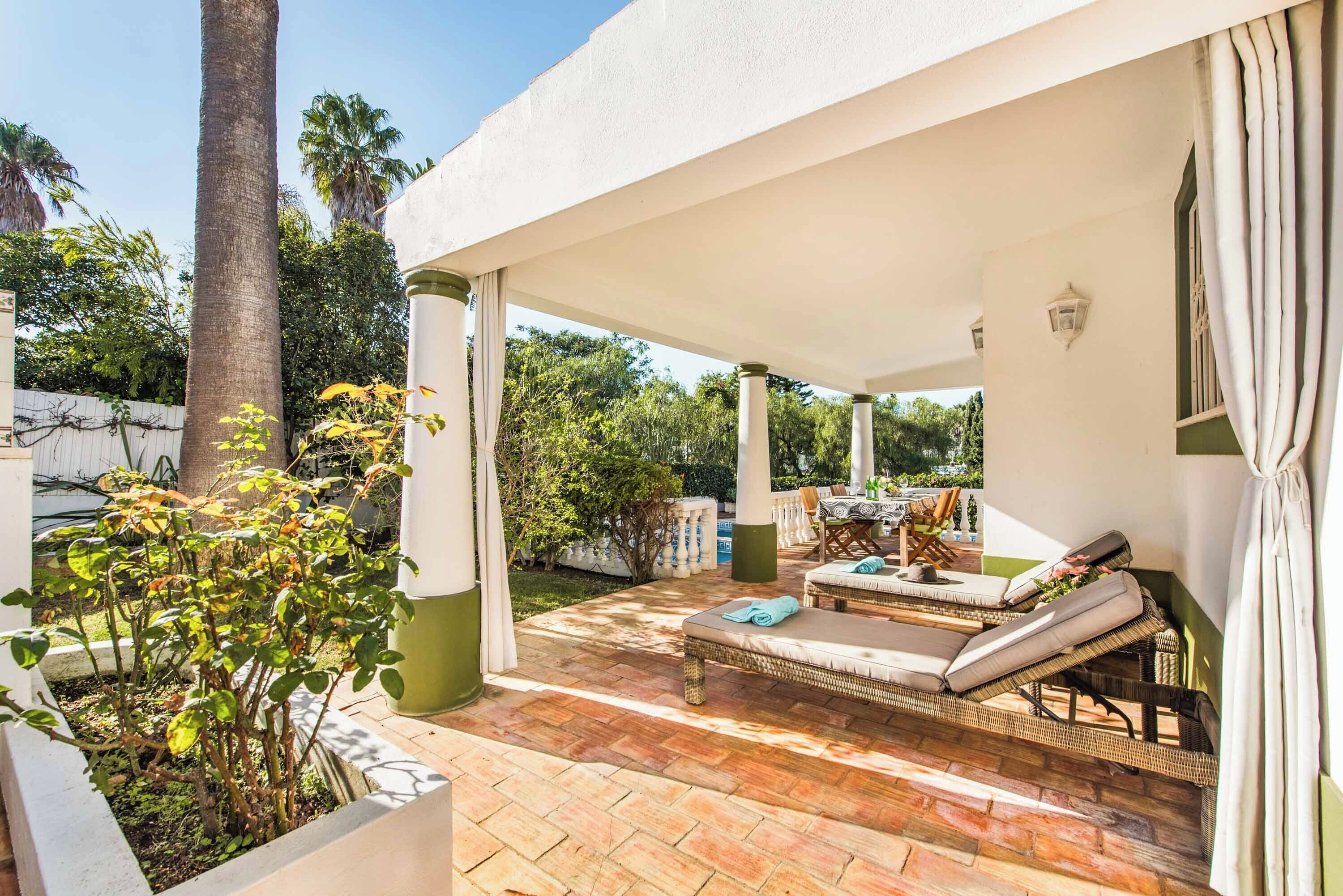 A covered patio with two lounge chairs, a table, and a small pool area.