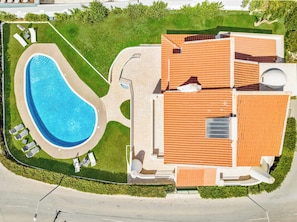 An aerial view of a property with a swimming pool, a covered patio area, and a building with a tiled roof. - Villa Corcovada (Albufeira)
