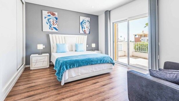 A modern bedroom with a large bed, a nightstand, a chair, and a balcony with a view. - Villa Corcovada (Albufeira)