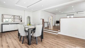 A modern kitchen with white cabinetry and a dining area with a wooden table and chairs. - Villa Corcovada (Albufeira)