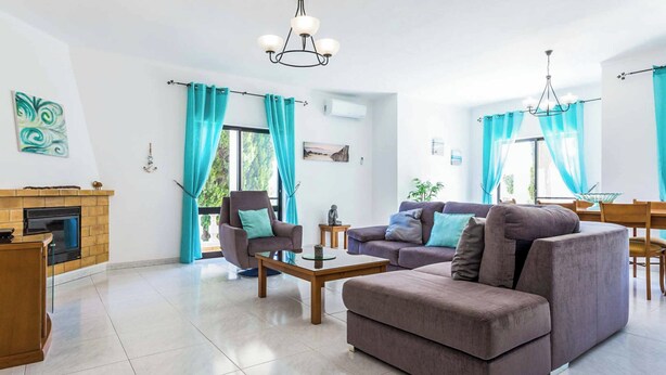 A modern living room with a fireplace, two sofas, a coffee table, and a dining area with a table and chairs. - Villa Bonita Gale (Albufeira)