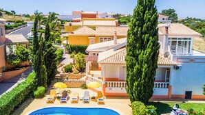 A residential area with a swimming pool, sun loungers, and a tall tree. - Villa Bonita Gale (Albufeira)