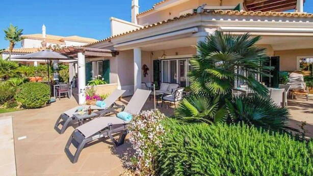Une maison dotée d’un patio aménagé avec des chaises longues et une table à manger.
