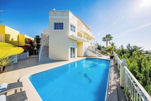 Une piscine, avec un bâtiment blanc attenant, doté d’un balcon et d’un escalier menant à un niveau supérieur.